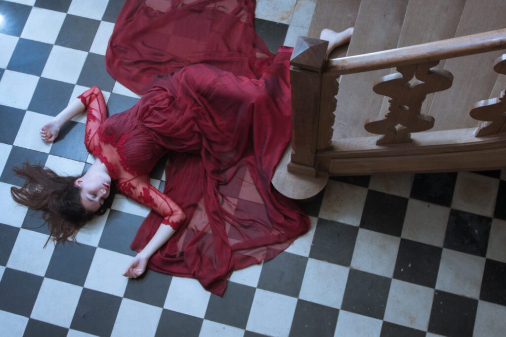 Photogrpahie d'une femme portant une robe rouge, évanouie au bas d'un escalier